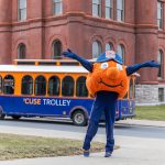 Otto, hands raised, in front of Trolley driving past Tolley Building.